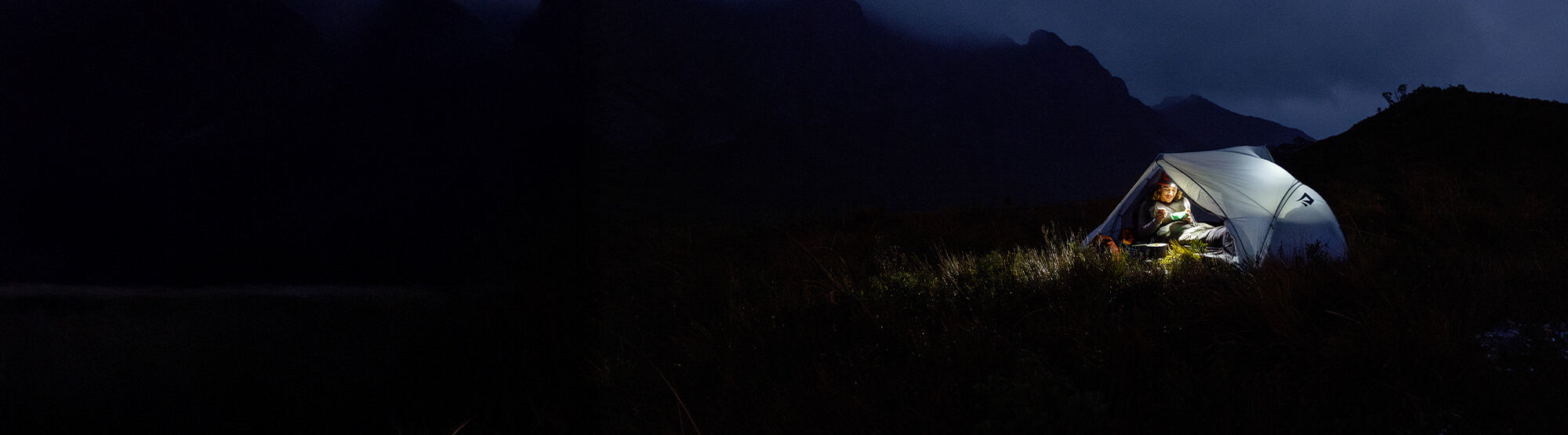 Person inside a illuminated tent in a mountainous area at night