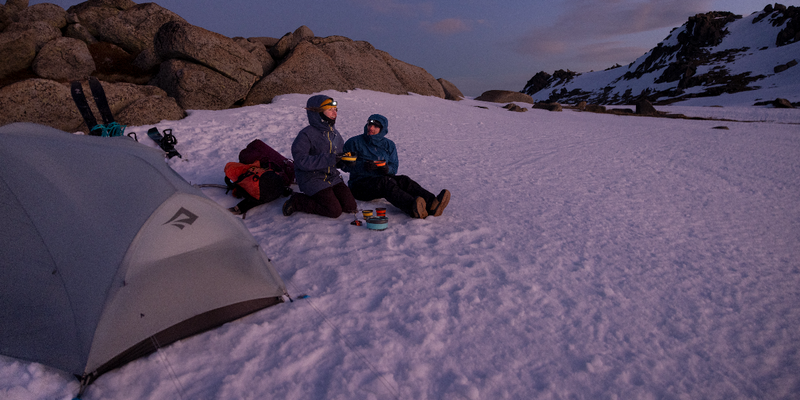 A couple of backcountry skiers laugh together at camp as they have dinner using ultralight collapsible dinnerware