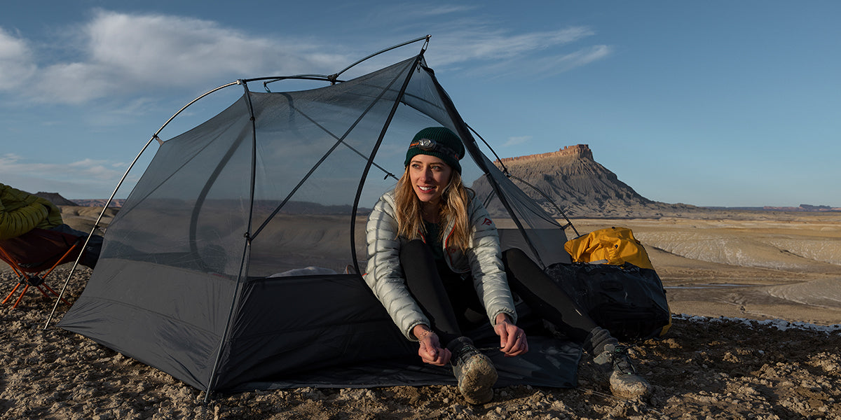 a girl sits in nature in an inner tent and laces up her shoes 