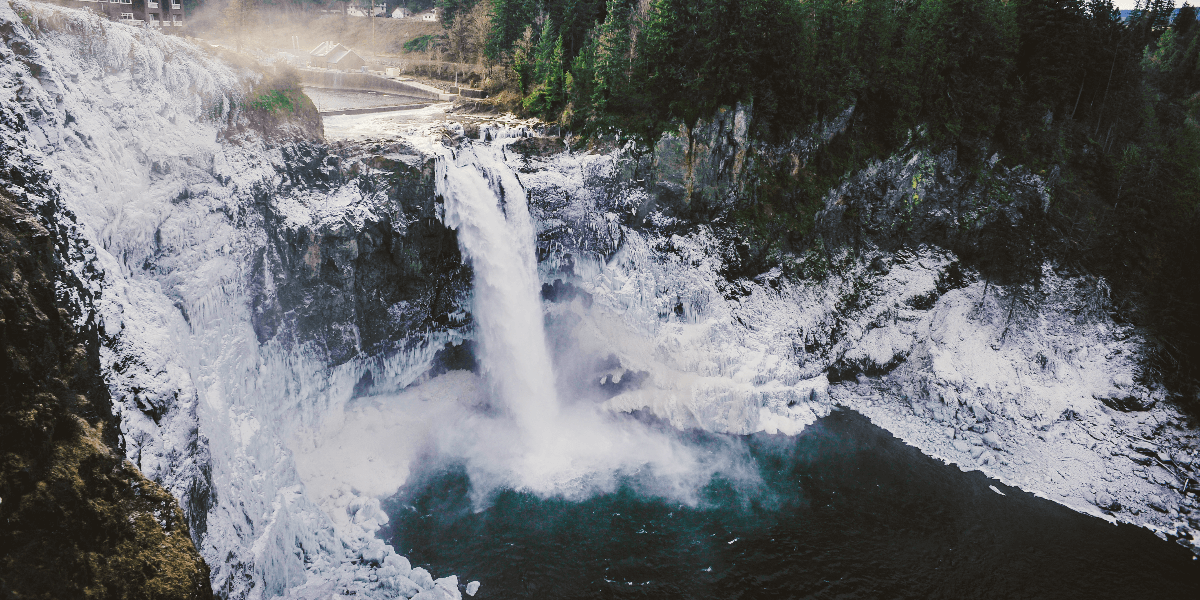 A birds eye view of a waterfall surrounded by snow and deep blue water