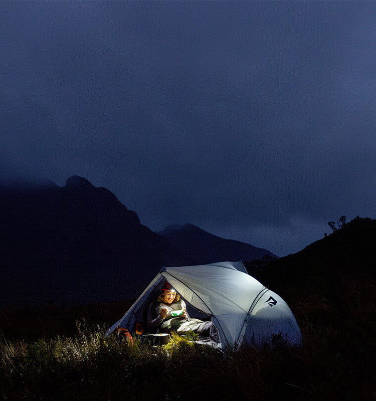 Person inside a tent with mountains in the background at night